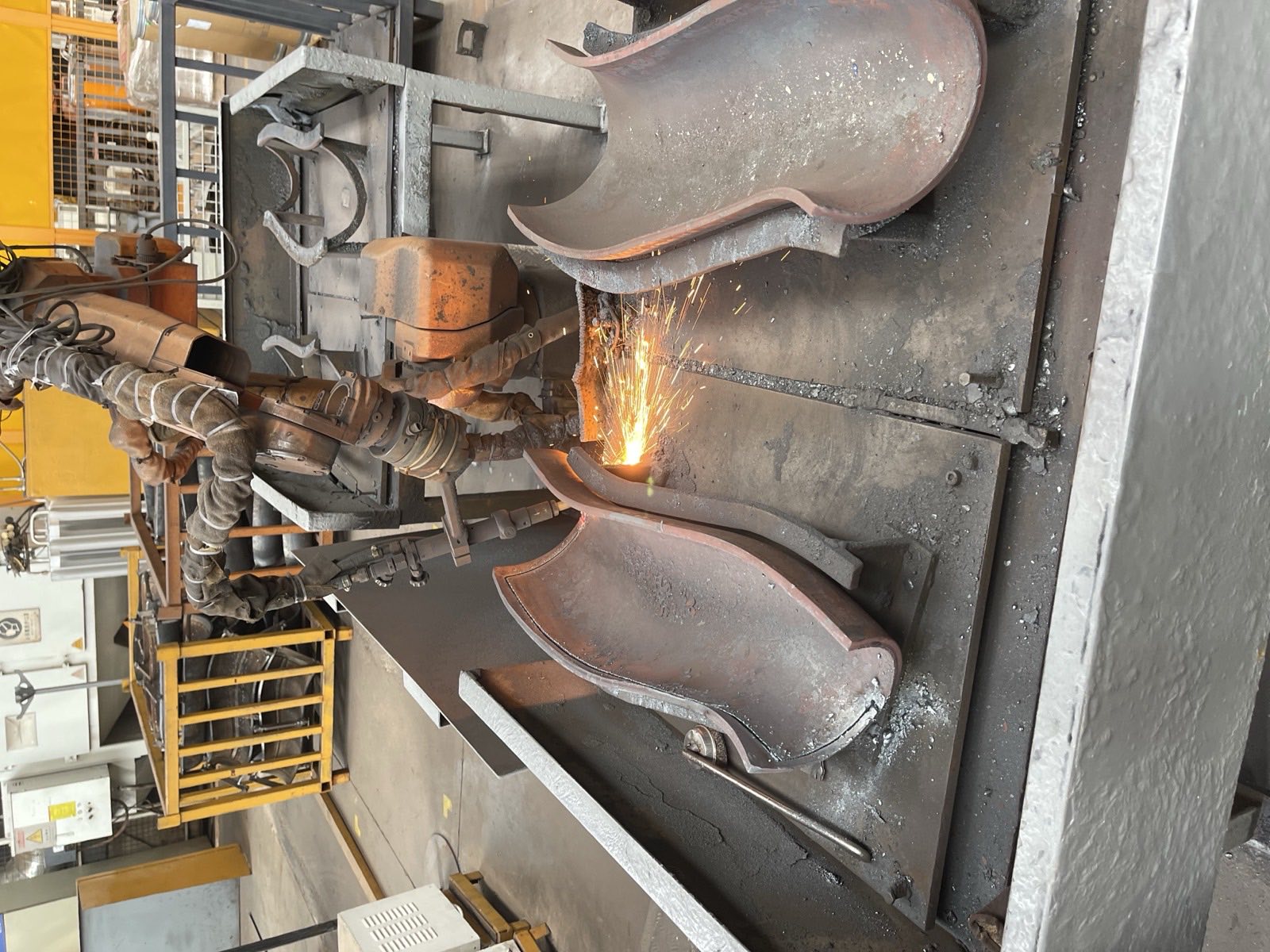 Automated hardfacing station laying overlay onto curved liner segments, sparks flying